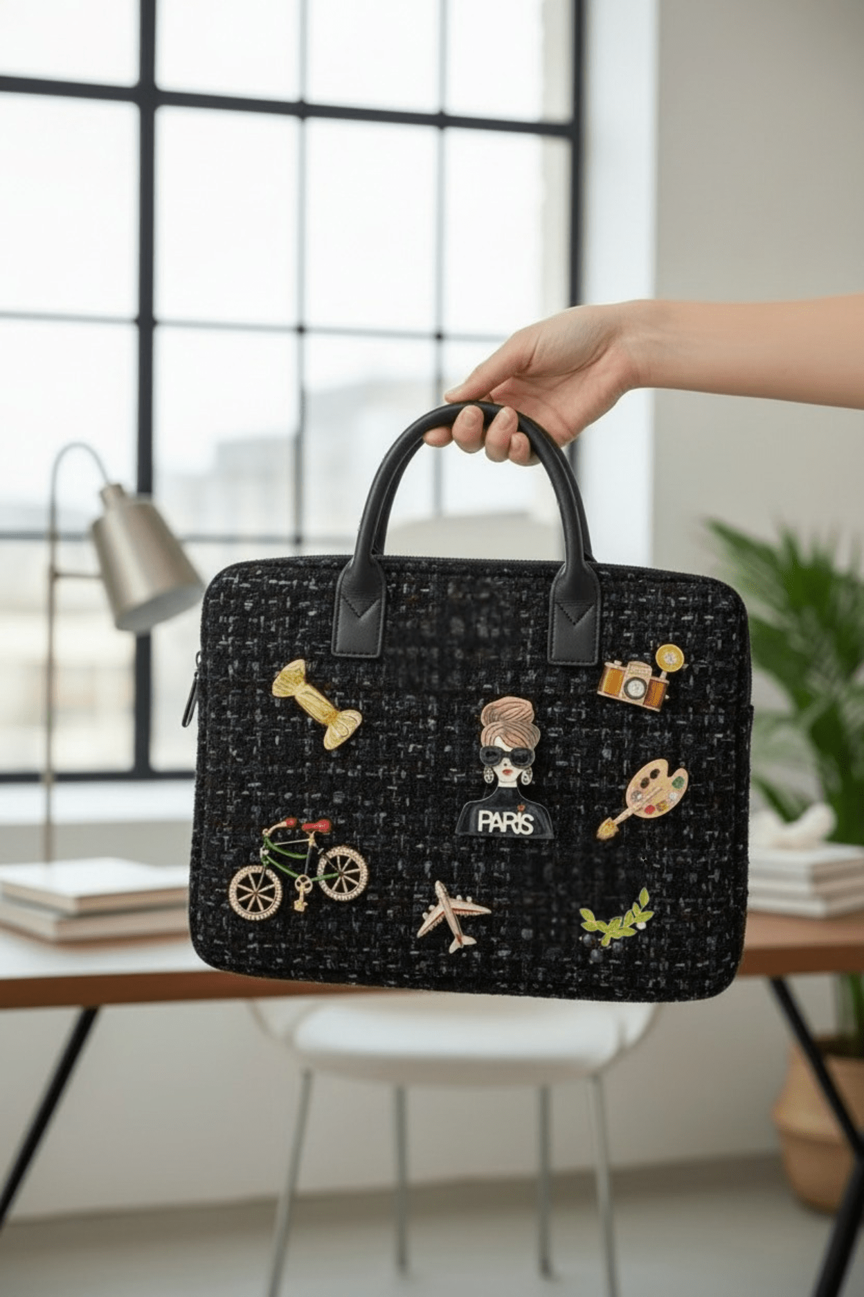 Black textured handbag with various pins held by a hand in an indoor office setting.