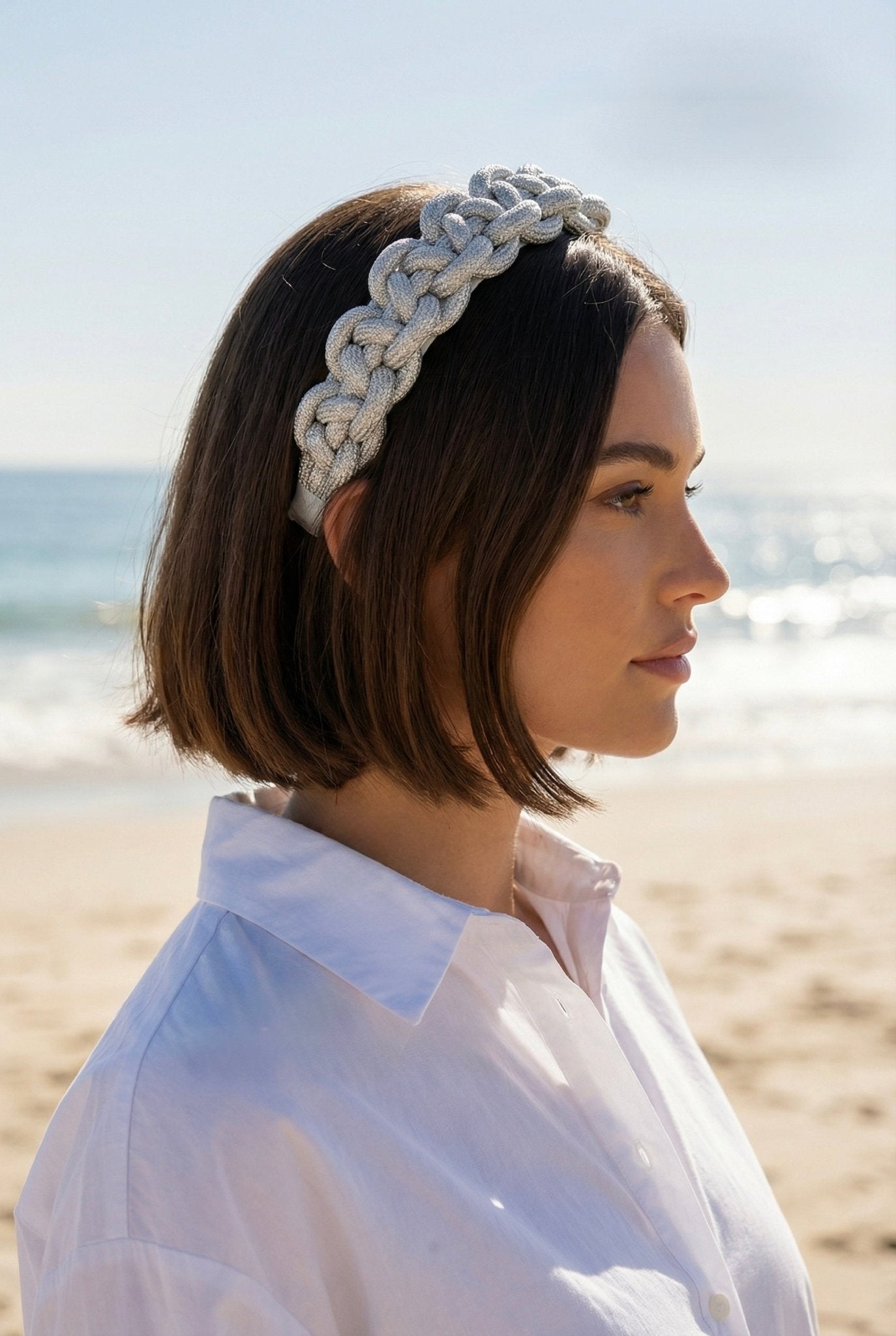 Woman with brunette hair wearing a silver braided headband on a beach