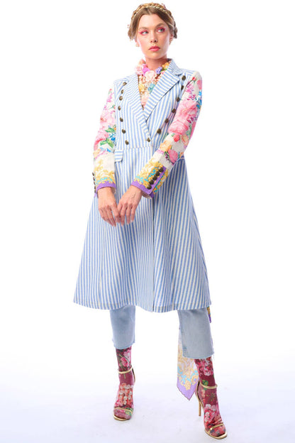 Woman wearing a blue and white striped coat with colorful floral print sleeves and antique gold button closure on a white background