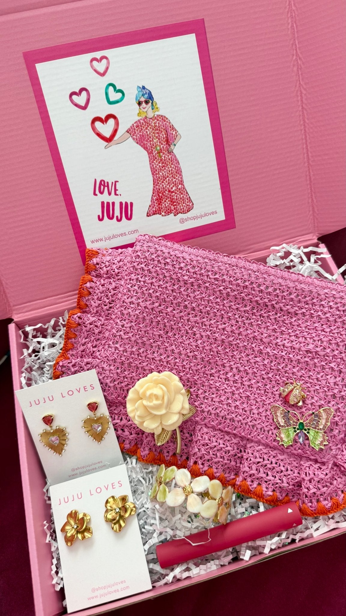 Pink Surprise Me JuJu gift box with earrings, a pouch, brooches, a cuff bracelet, and lip gloss with crinkle paper.