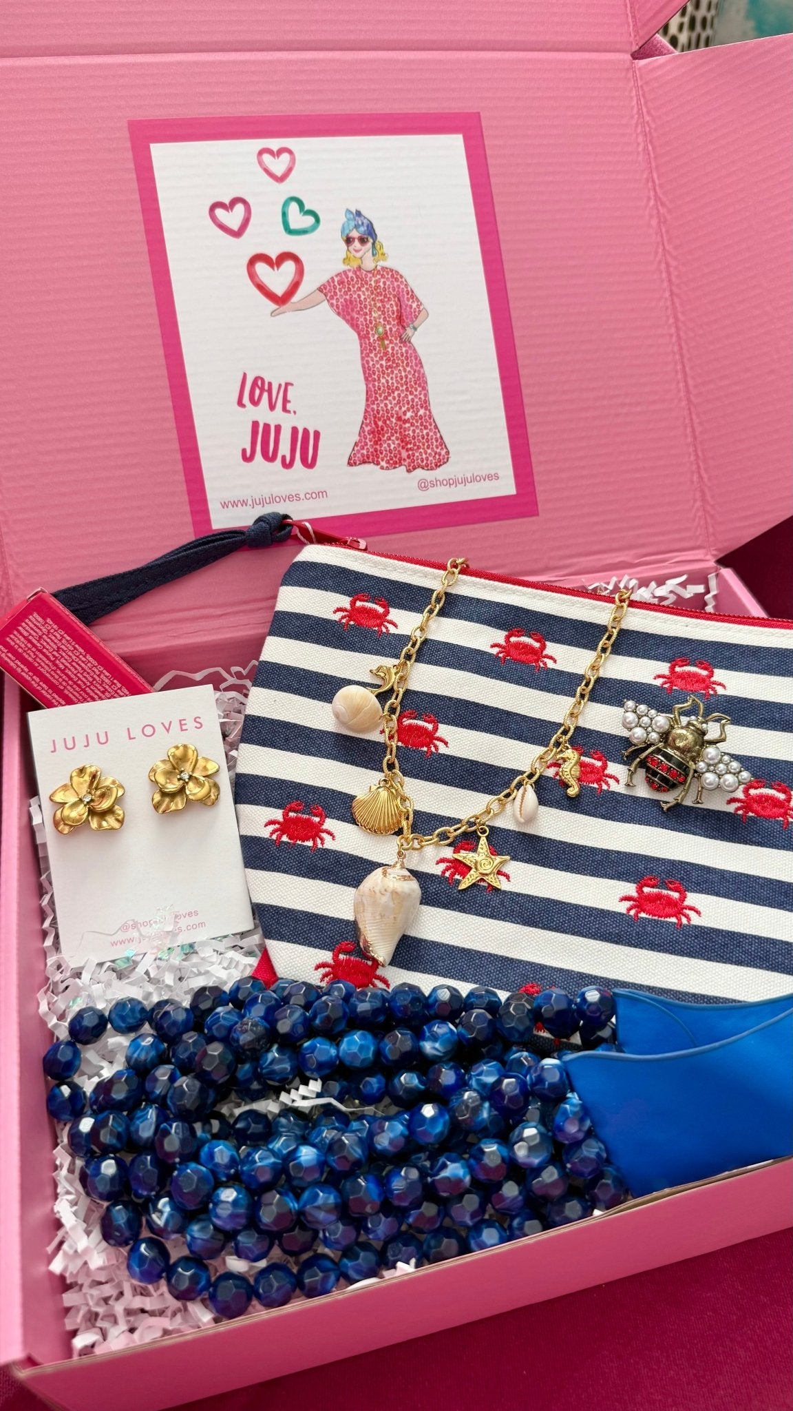 Pink Surprise Me JuJ Gift Box with necklace, earrings, a pouch, and a brooch with white crinkle paper and a "love JuJu" sticker on the box.
