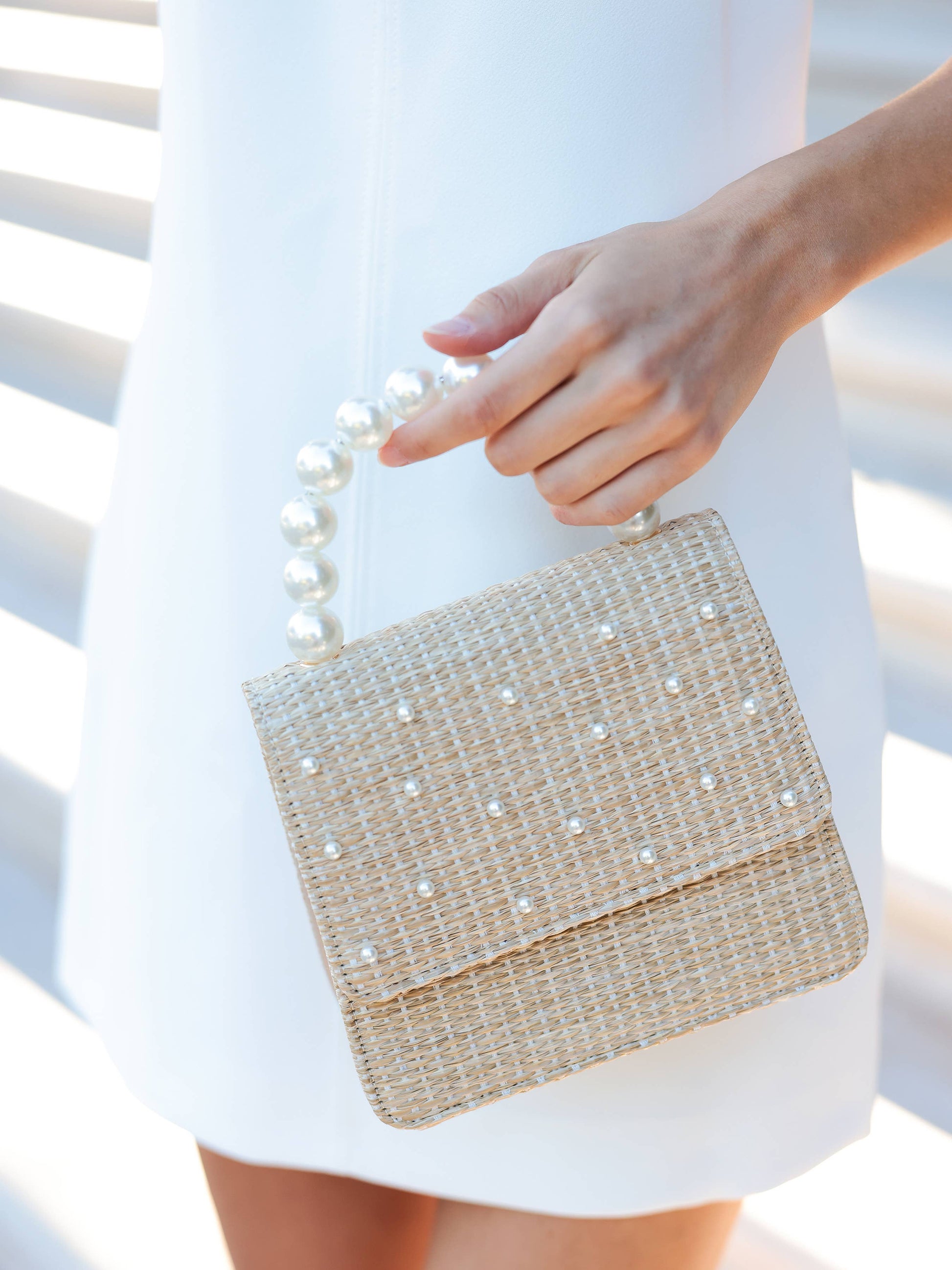 up close mage of woman holding raffia and pearl handbag with faux pearl detailing and pearl handle
