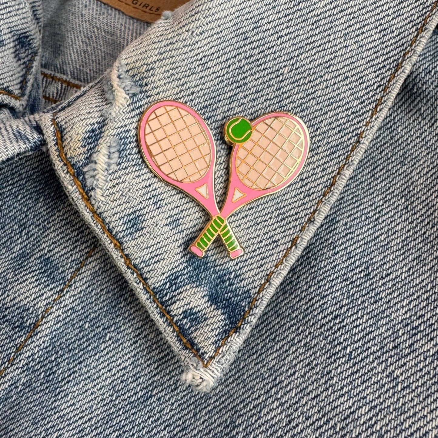 Pink tennis racket and ball enamel pin on a denim jacket