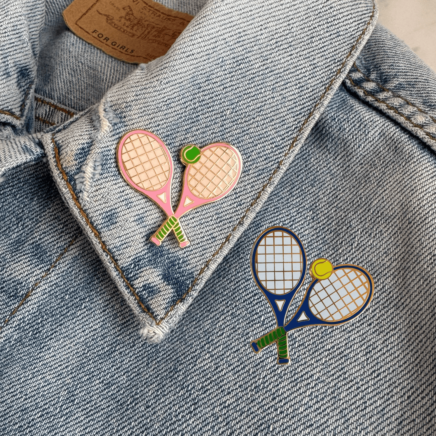 Two colorful tennis racket pins on a denim jacket.
