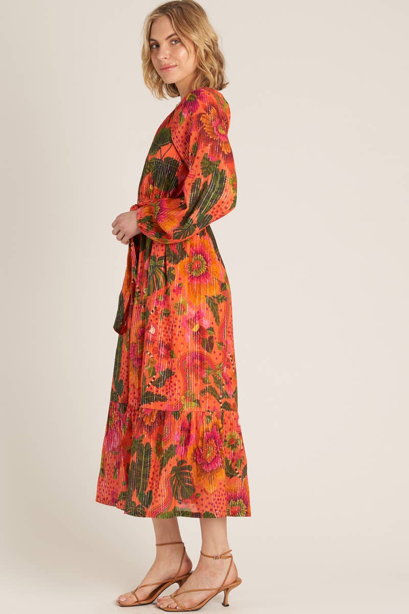 side view of woman wearing a one shoulder orange tropical print dress and strappy heels