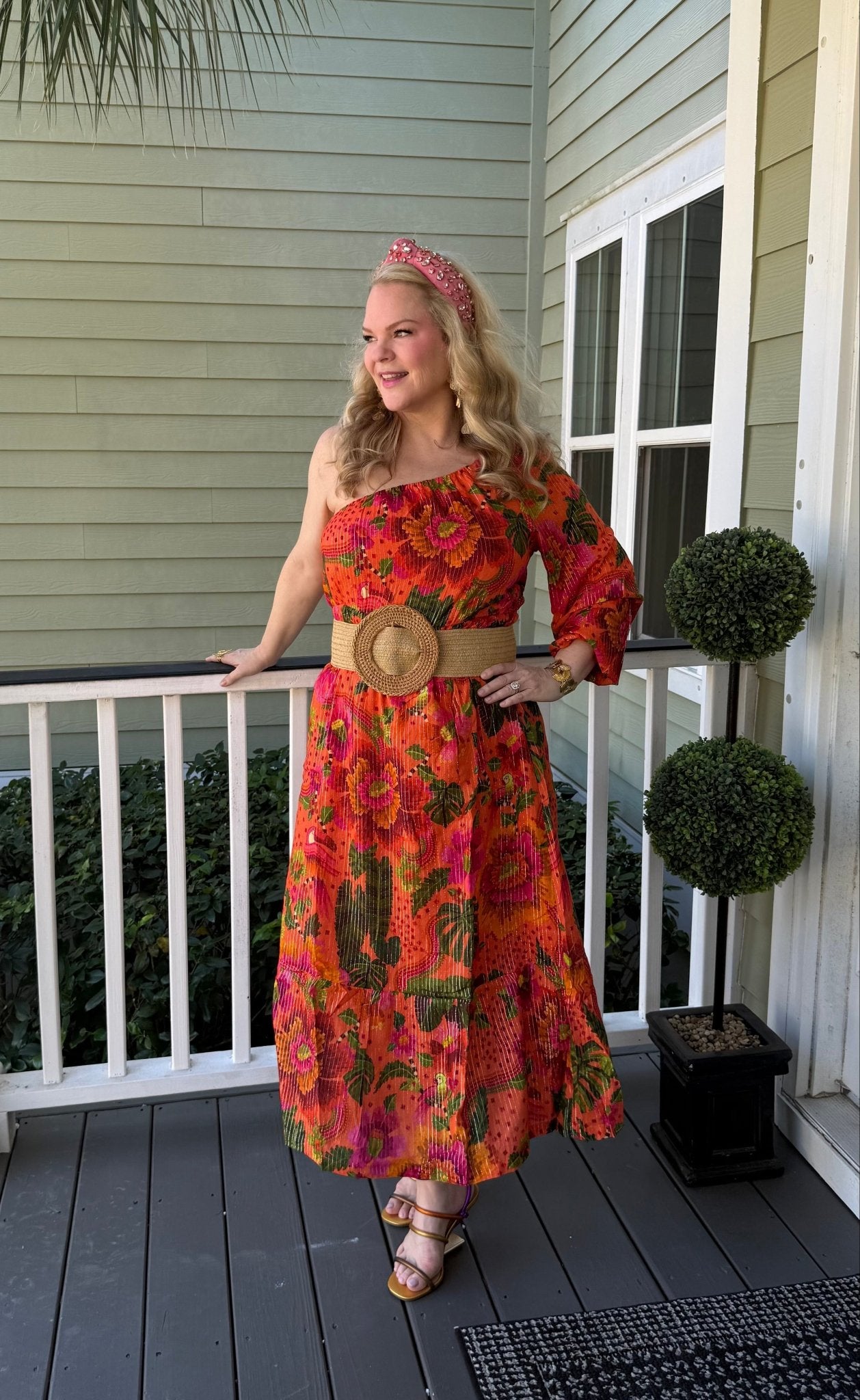 Woman in a one shoulder orange floral dress standing on a porch