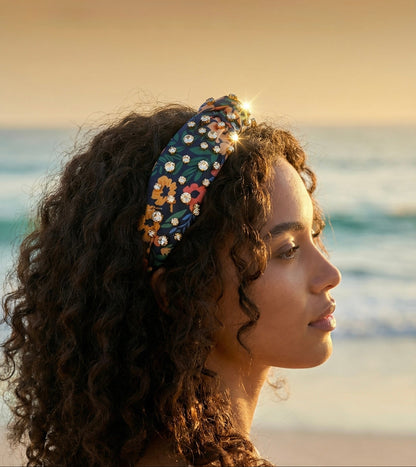 Woman with a rhinestone embellished floral headband looking out at the ocean during sunset.