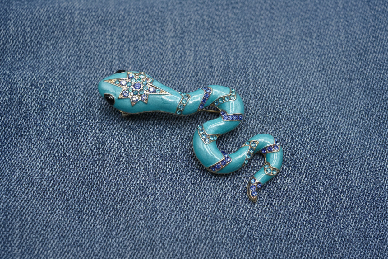 Decorative blue snake-shaped brooch with gemstone accents on a denim fabric background