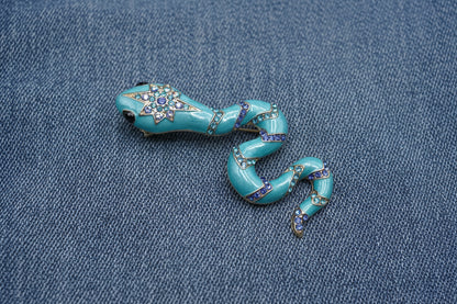 Decorative blue snake-shaped brooch with gemstone accents on a denim fabric background
