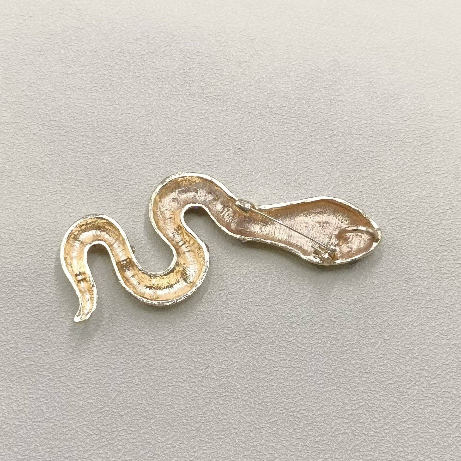 Back view of snake-shaped brooch with silver color on a light gray background