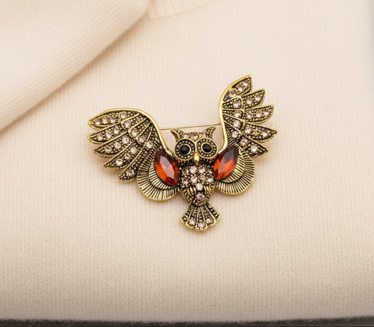 Gold owl brooch with red gemstones on an ivory fabric background