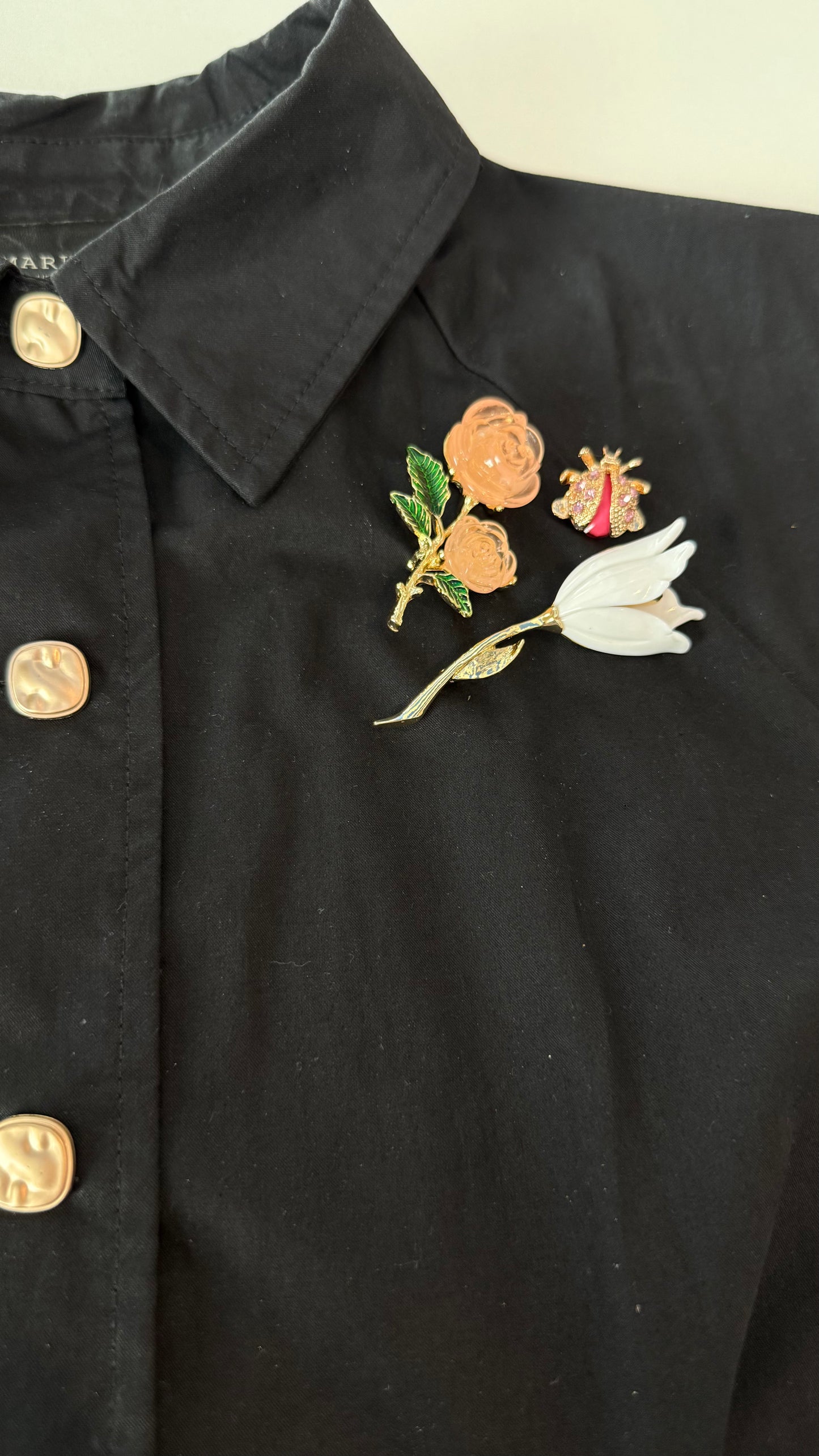 Black jacket with floral brooches on a plain background including a rose, tulip, and bee