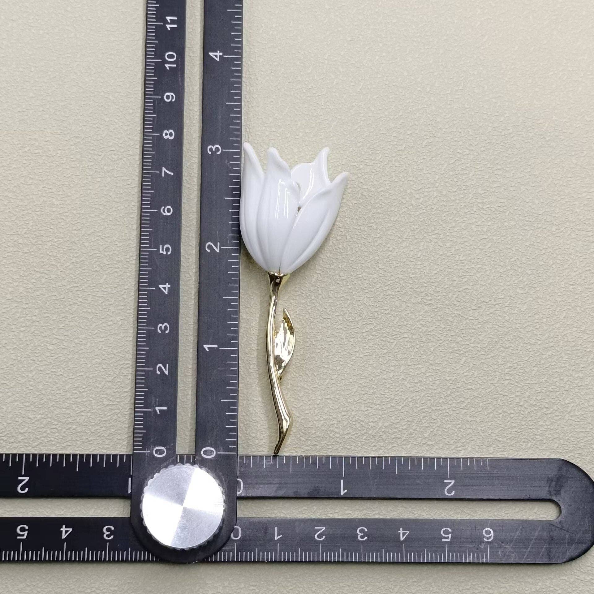 White tulip-shaped brooch next to a ruler for scale on a beige background