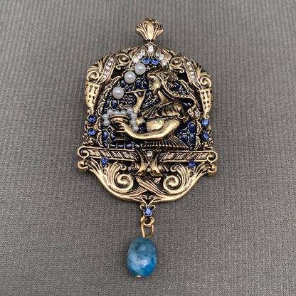 Decorative pendant with intricate design and blue gemstone on a gray background