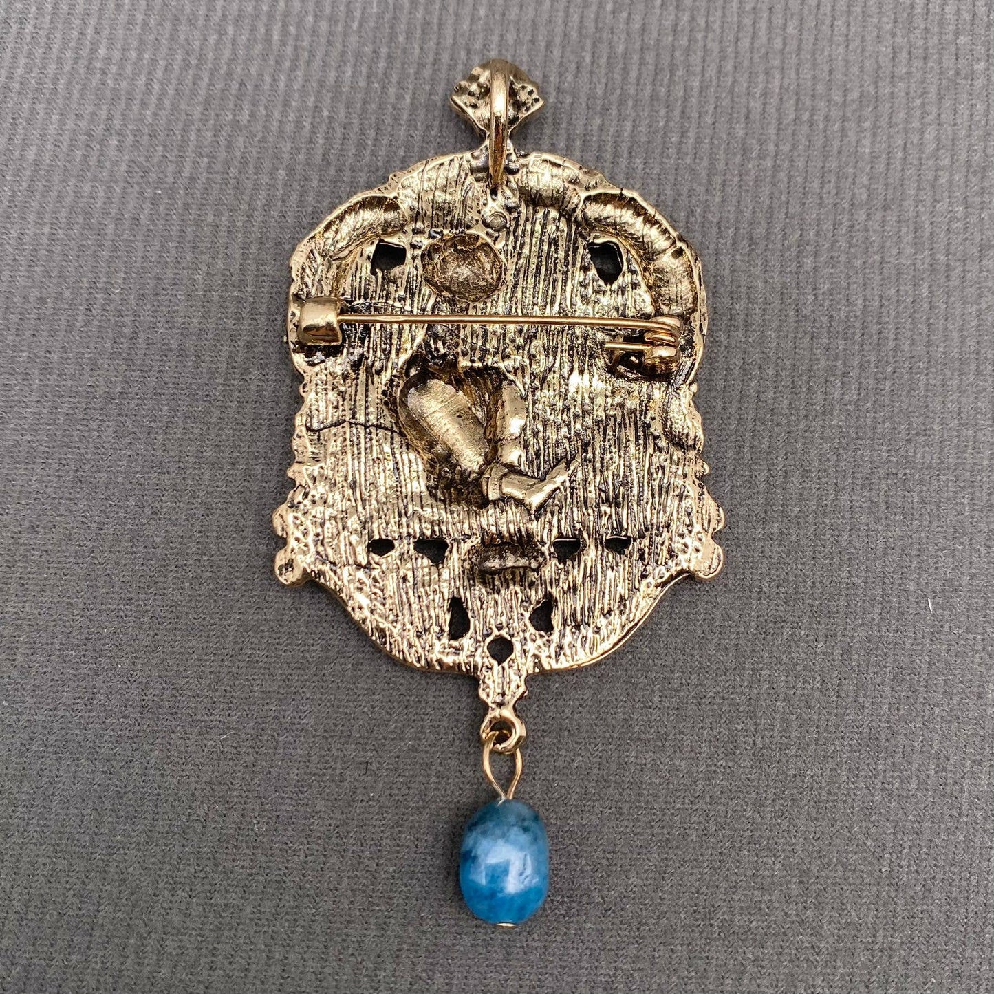 back view of Decorative brooch with intricate design and blue stone on a gray background