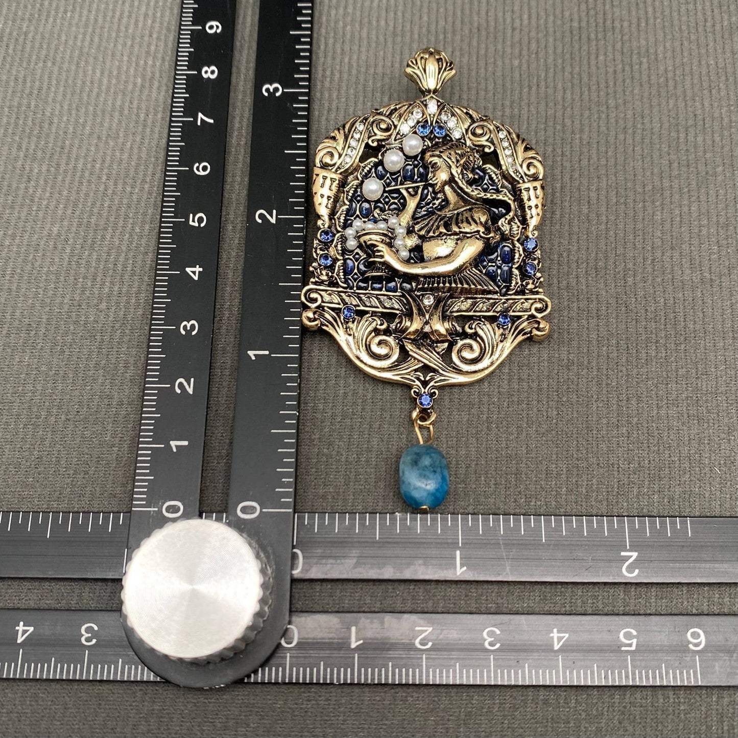 Decorative brooch with blue stone on a ruler for scale