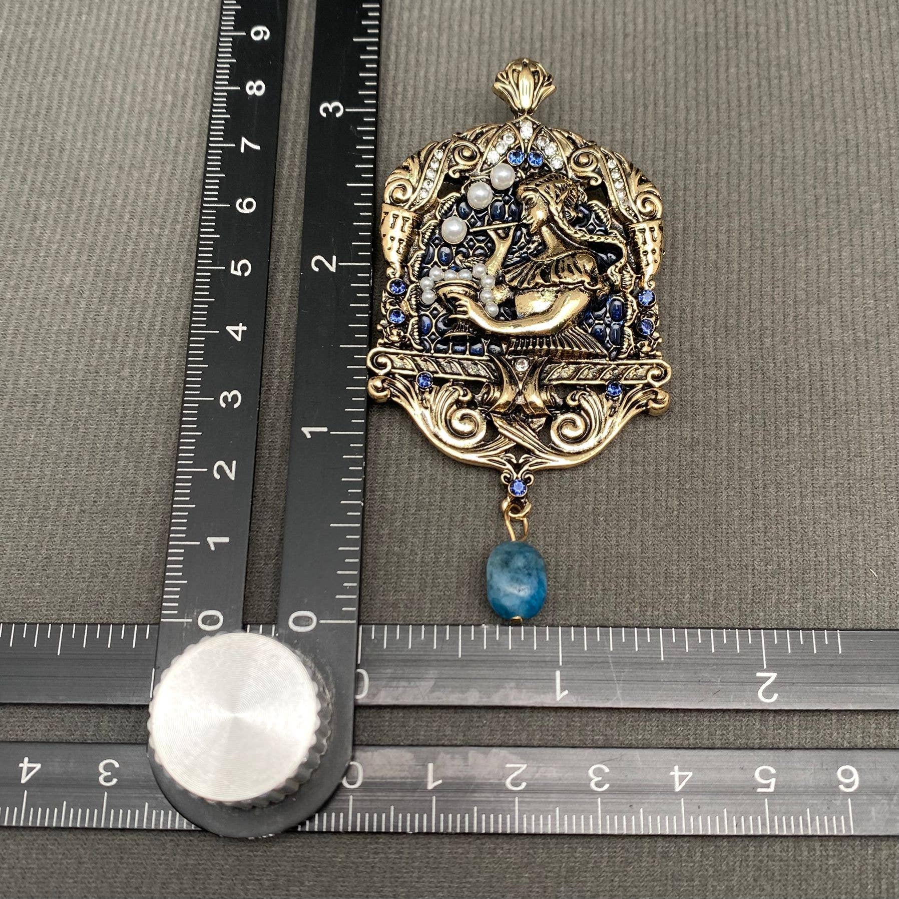 Decorative brooch with blue stone on a ruler for scale