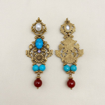 Ornate earrings with turquoise and red beads on an ivory background