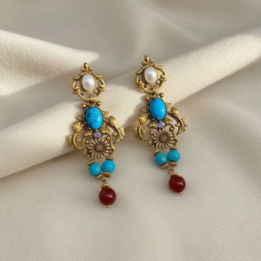 Pair of ornate earrings with turquoise and red beads on an ivory background