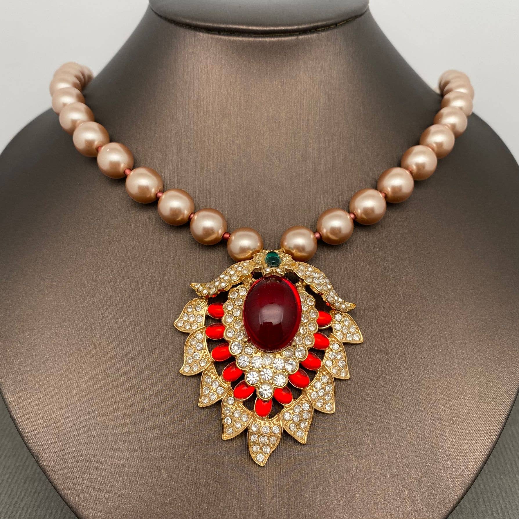 Pearl necklace with a decorative pendant featuring a red gemstone on a mannequin.