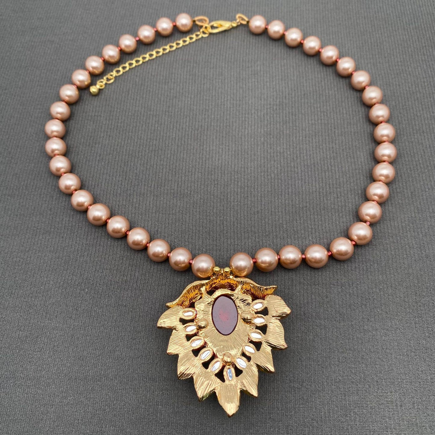 Back view of a pearl necklace with a gold pendant on a gray background