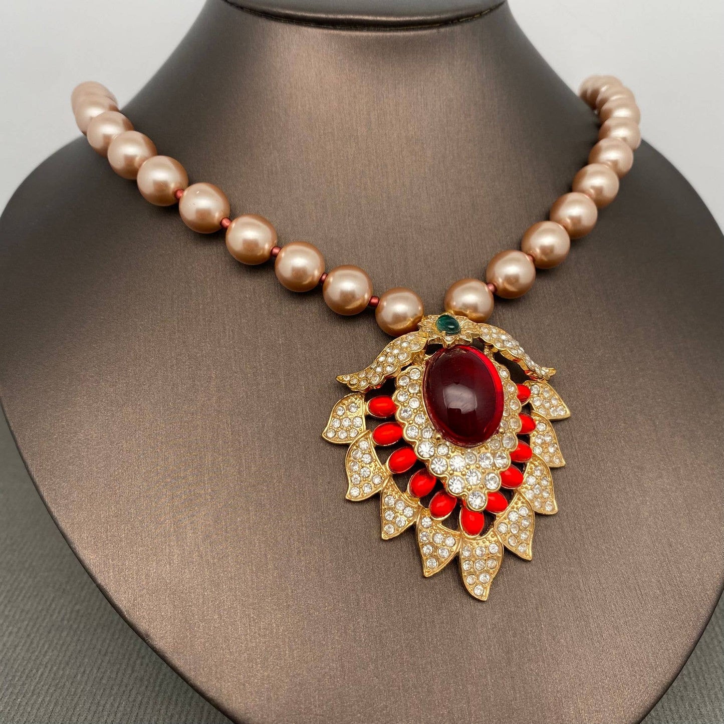 Pearl necklace with a decorative pendant featuring a red gemstone on a mannequin.