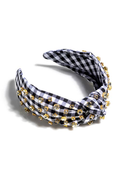 A black and white gingham knotted headband with multicolored rhinestone details laying on a white surface
