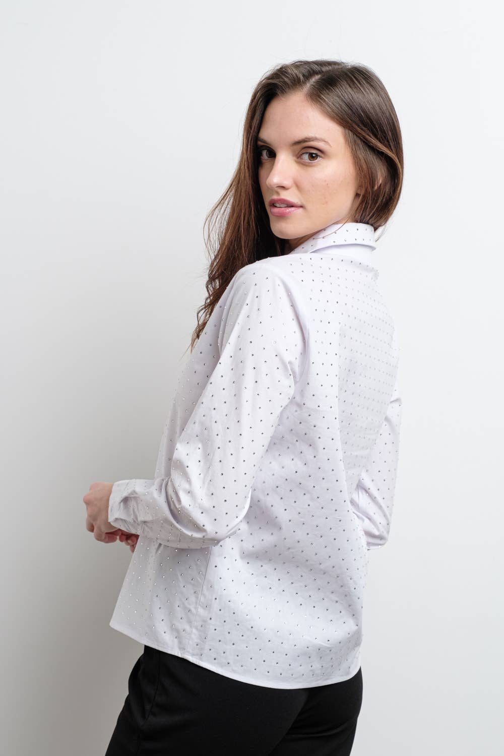 Woman wearing a white blouse with a rhinestone pattern on a plain background