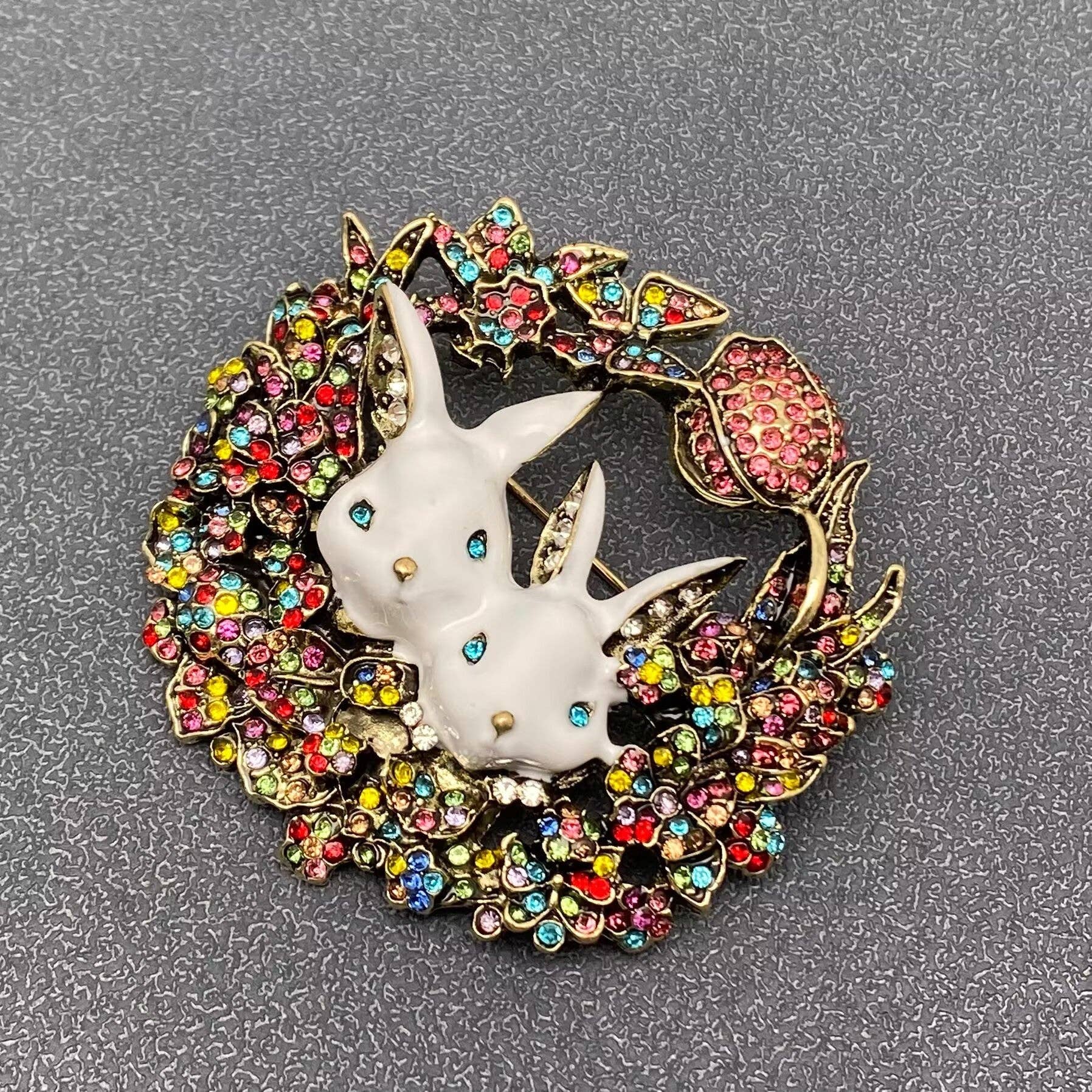 Decorative brooch with a rabbit design surrounded by colorful gemstone wreath on a gray background