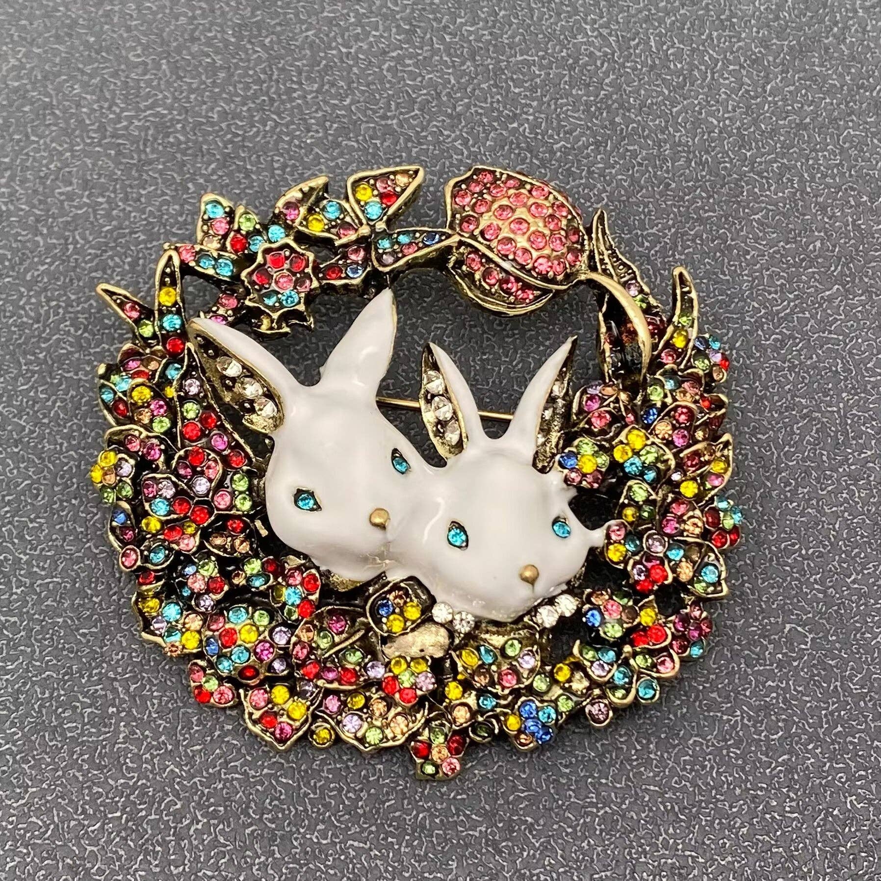 Brooch with two white rabbits in a colorful wreath on a gray background