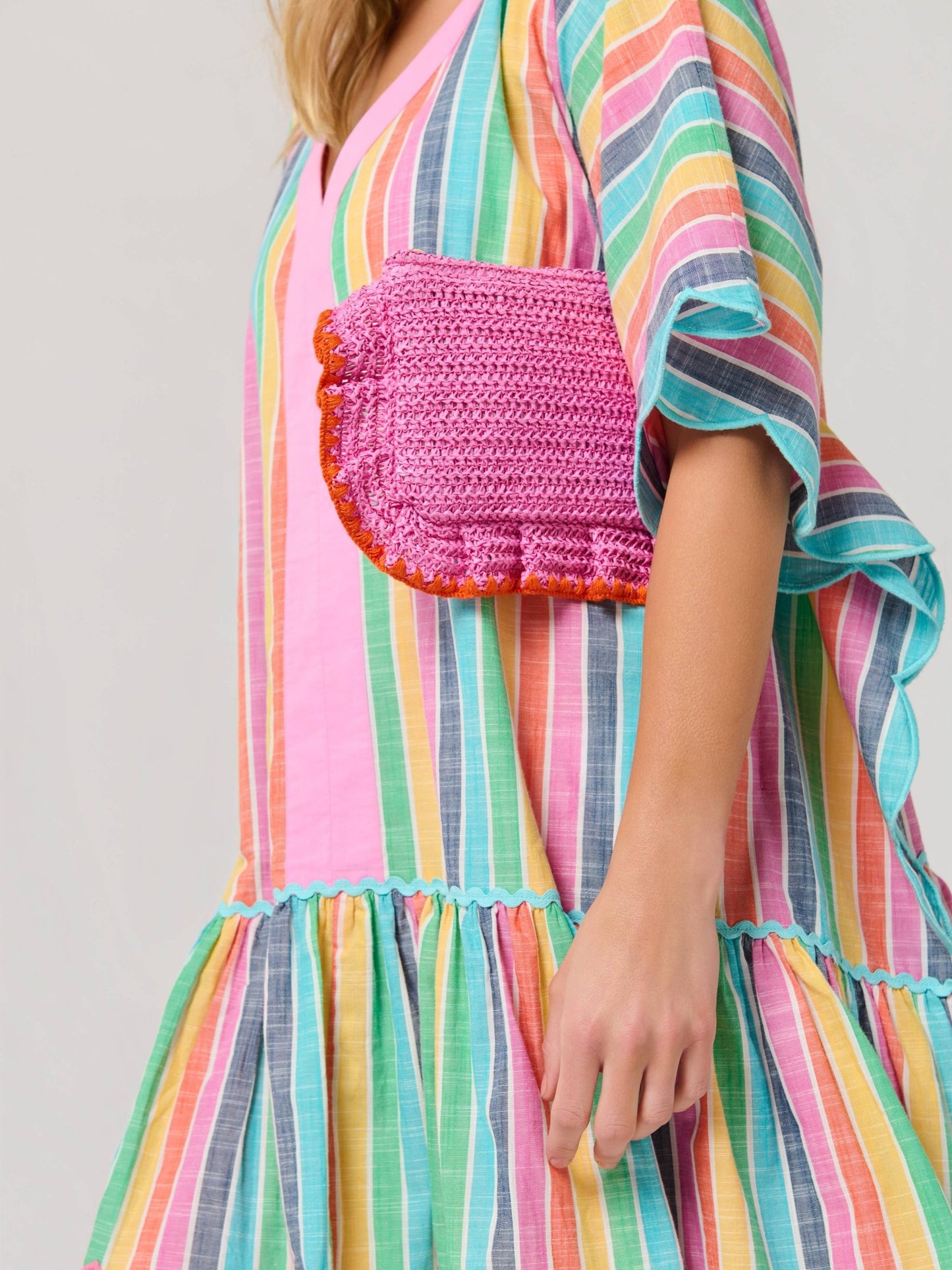 Person wearing a colorful striped dress with a pink woven bag on a plain white background