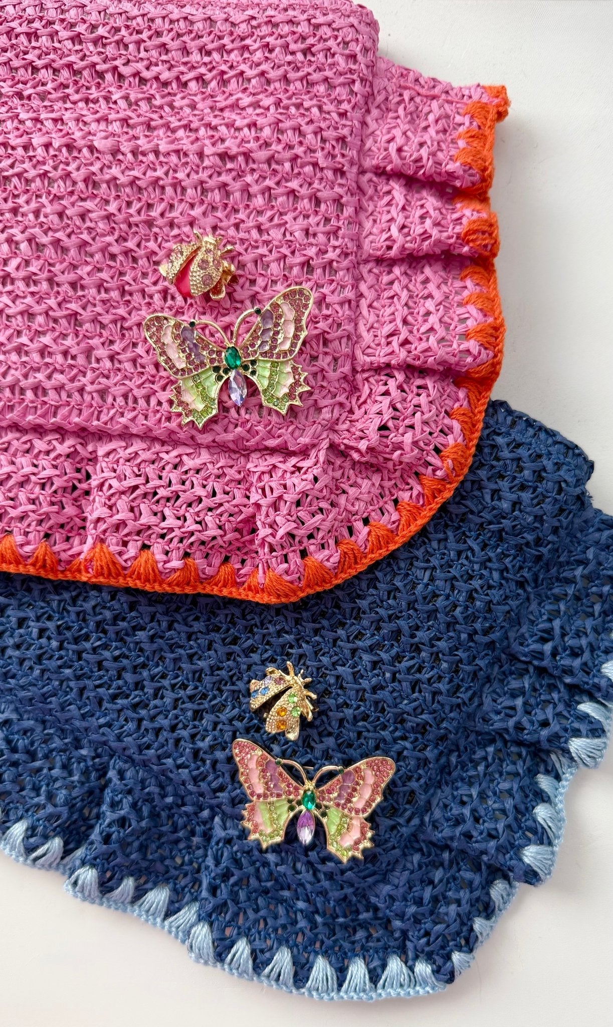 Two crocheted clutches, one pink and one blue, with butterfly and ladybug brooches on a white background.