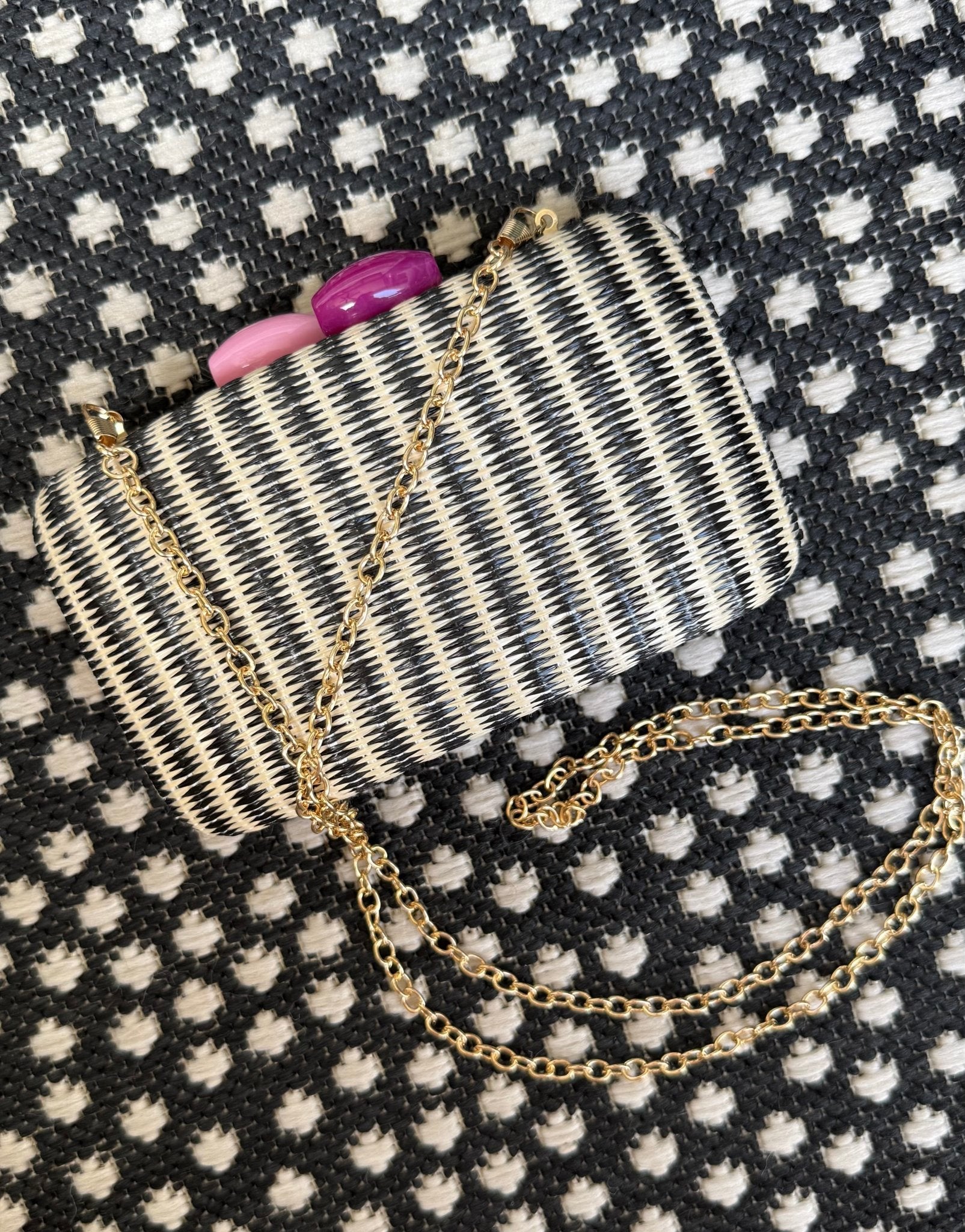 Small woven black stripe handbag with a chain strap on a patterned fabric background