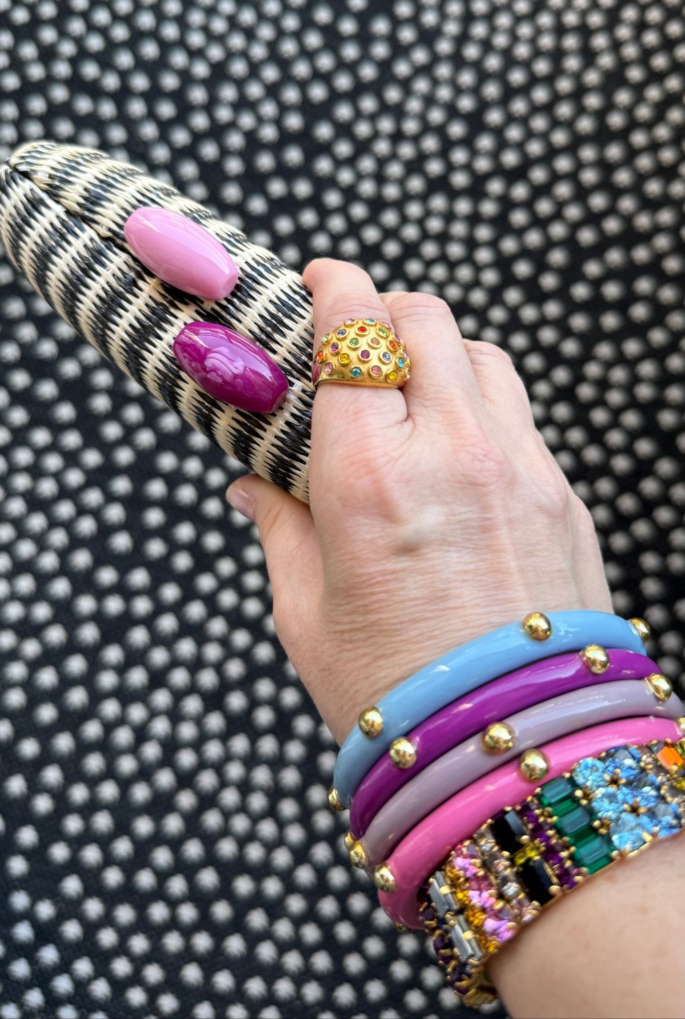 Hand wearing colorful bracelets and rings holding a black stripe woven clutch on a textured black and white background